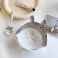 an animal shaped bowl next to a spoon on a white table with other items around it