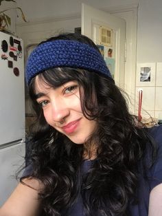 a woman with long hair wearing a blue headband and smiling at the camera while standing in front of a refrigerator