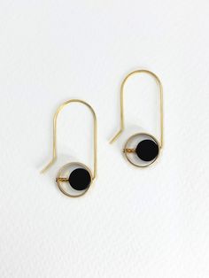 Golden brass and semi precious stones of Onyx are paired together in these geometric dangle earrings.  The matte black onyx stones, with their deep, velvety hue, compliment the warmth of the polished brass.  The brass gleams softly against the smooth surface of the onyx and the contrasting textures and tones create visual impact.  A rounded edge brass frame surrounds a coin shaped stone as a block of three small, gold plated, glass seed beads position it off centre.  Approximate measurements- 4c Minimalist Round Brass Earrings, Modern Gold Earrings With Black Enamel, Modern Black Round Hoop Earrings, Minimalist Black Pierced Jewelry, Minimalist Geometric Pierced Jewelry, Minimalist Black Single Earring, Minimalist Black Metal Jewelry, Minimalist Geometric Jewelry, Modern Black Single Earring