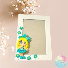 there is a photo frame with a doll in it and flowers on the table next to it