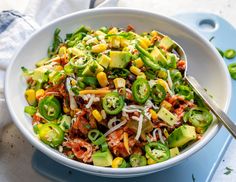 a white bowl filled with vegetables and cheese on top of a blue tray next to a fork