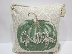 a decorative pillow with the word grateful on it and a green pumpkin sitting on top