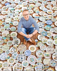 a man sitting on top of a wooden table surrounded by lots of different types of plates