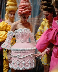 a group of women standing next to each other in front of a pink cake on top of a table