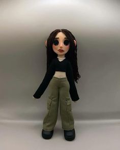 a doll with long brown hair and black sweater standing in front of a gray background