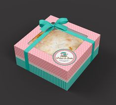 a pink and green box with a bow on the top that has a piece of cake in it