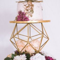 a three tiered cake with pink flowers on the top and gold geometric stand above it