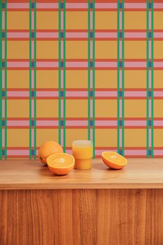 three oranges sitting on top of a wooden counter next to a wall with colorful stripes