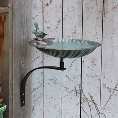 a metal bird bath sitting on top of a stand next to a wooden wall with peeling paint