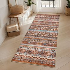 an orange and blue area rug in a room with white walls, wooden flooring and potted plants