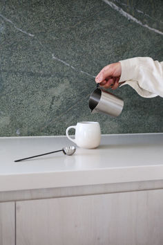 a person pours coffee into a cup on a counter top with a marble wall behind it