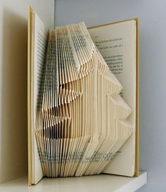 an open book with folded pages sitting on top of a shelf