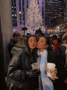 two women standing next to each other in front of a christmas tree with lights on it