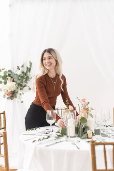 a woman sitting at a table with flowers and wine glasses in front of her smiling