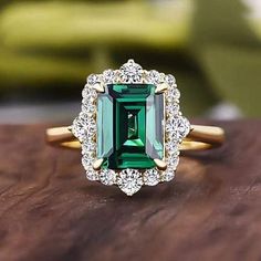 an emerald and diamond ring sitting on top of a wooden table next to a couch