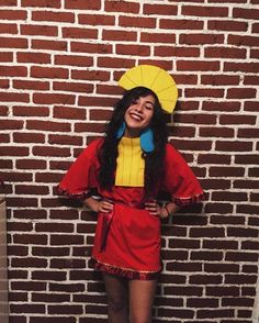 a woman standing in front of a brick wall wearing a red and yellow dress with an umbrella over her head