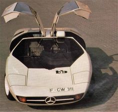 an aerial view of a white car with its hood open and the front lights on