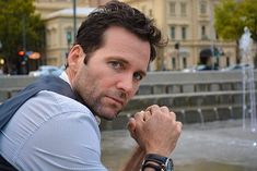 a man is posing in front of a fountain with his hand on his chin and looking at the camera