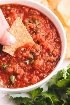 a hand holding a tortilla chip and dipping it into a bowl of salsa