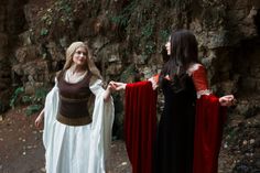 two women dressed in medieval costumes standing next to each other on a path near a cliff