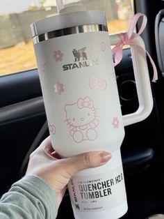 a person holding up a hello kitty tumbler in their car with a pink bow on it