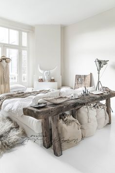 a white bedroom with a large wooden bench in the middle and pillows on the floor