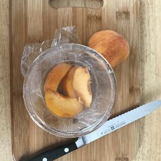 two pieces of peach sitting on top of a wooden cutting board next to a knife