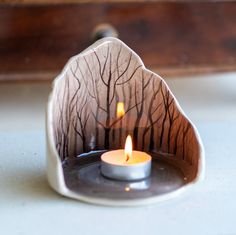 a lit candle in a bowl with trees on it