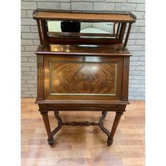 an old fashioned wooden cabinet with mirror on it's top and bottom shelf, in front of a brick wall