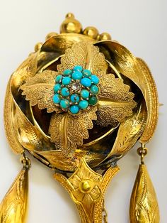 A stunning and eye catching piece of jewellery which is very evocative of its period C1830.  3.5 by 1.5 inches. Does not sound that large  but measure other brooches in your collection to compare. It could convert to a pendant and either way it is quite exceptional. The back holds a large empty locket compartment and most unusually, the gold bound glass is easy to take out and reinsert.  It would have held the hair of a loved one but these days it can hold whatever you want. The central boss is decorated with beads of turquoise with a rose cut diamond to the centre.  The boss is set amongst four veined and textured leaves . These in turn are encircled by a ribbon of gold engraved with leaves. The sides are extended slightly by two curves of gold from which descend two gold torpedos.  The c Traditional Yellow Gold Collectible Brooch, Traditional Yellow Gold Pendant Brooches, Turquoise Brooch For Formal Occasions, Victorian Ceremonial Brooch, Victorian Cabochon Ceremonial Jewelry, Antique Medallion Brooch Jewelry, Antique Blue Jewelry With Brooch, Antique Brooches With Intricate Design For Ceremonial Use, Antique Ceremonial Brooches With Intricate Design