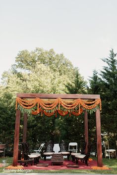 an outdoor wedding ceremony setup with orange flowers and greenery on the arbor, surrounded by trees