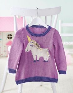 a purple sweater with a unicorn on it is hanging from a white chair in front of a doll house