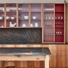 a kitchen with wooden cabinets and marble counter tops, along with red glass cabinet doors