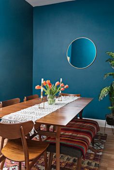 a dining room with blue walls and wooden table surrounded by colorful rugs, potted plants and chairs