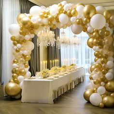 a long table with gold and white balloons on the wall next to a chandelier