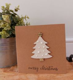 a card with a white christmas tree on it next to a potted green plant