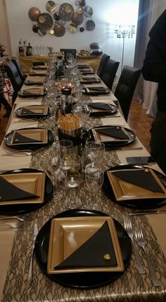 the table is set with black and gold plates, silverware, and napkins