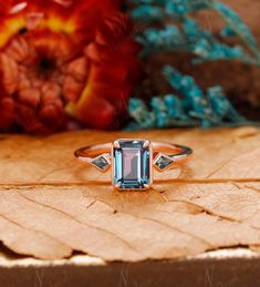 a ring with an aqua blue topazte surrounded by leaves and flowers on a wooden surface