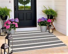 three potted flowers sit on the front steps of a white house with black and white striped rug