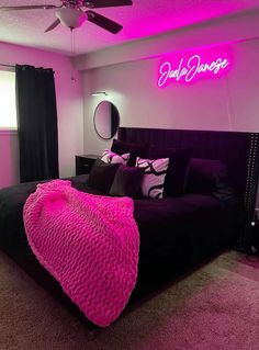 a bedroom with pink lighting and black bed in the corner, along with a neon sign