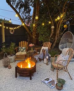 a fire pit surrounded by chairs and lights in a back yard with gravel flooring