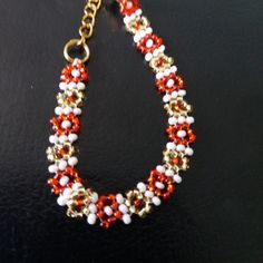 a red and white beaded bracelet on a black surface with gold chains, beads and clasps