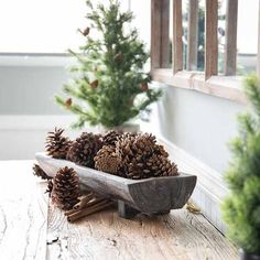 pine cones are in a wooden bowl on a table next to christmas trees and other decorations