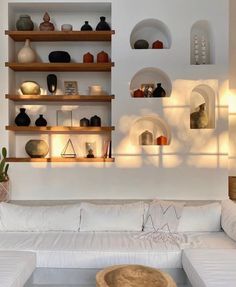 a living room filled with white furniture and lots of shelves on the wall above it