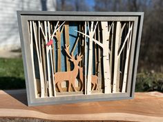 a wooden cut out of wood with deer and trees in the background, sitting on top of a piece of wood