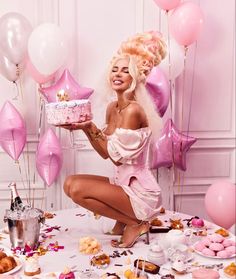 a woman kneeling down in front of a table filled with pink balloons and desserts