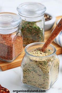 three jars filled with spices on top of a wooden cutting board next to other containers