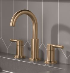 a gold faucet with two handles on a gray tiled wall next to a sink