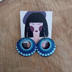 a pair of blue and white beaded earrings on top of a wooden table next to a card