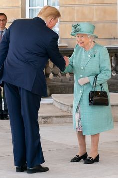 a man in a suit and tie shaking hands with an older woman wearing a blue dress